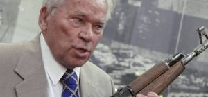 Elderly man holding a rifle, speaking.