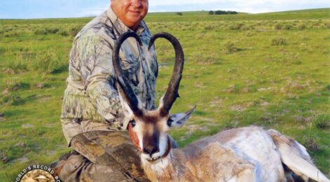 Hunter with antelope in grassy field.
