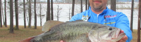 Man in blue cap holding a large fish by a lakeside.