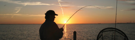 Silhouette of a person fishing at sunset by the water.