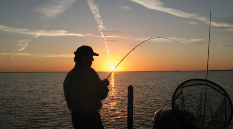 Silhouette of a person fishing at sunset by the water.
