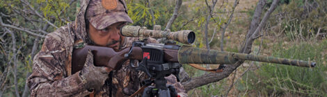Hunter aiming a rifle with camouflage in a forest.