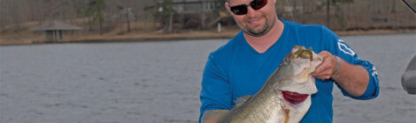 Man in blue sweater holding a large fish by a lakeside.