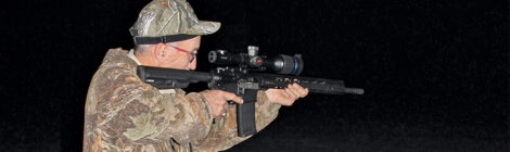 Man aiming a rifle equipped with a scope at night.