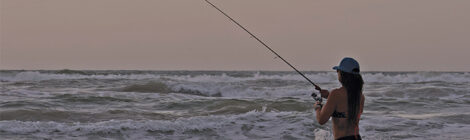 Person fishing at sunset on a beach with calm waves.