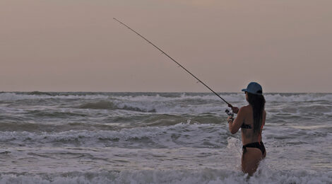 Person fishing at sunset on a beach with calm waves.