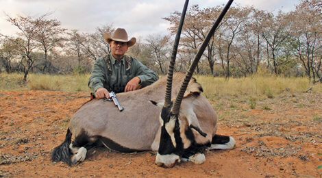 Hunter posing with a hunted oryx in a natural setting.