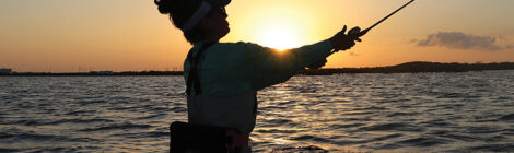 Person fishing at sunset, casting a line into the water.