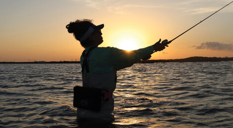Person fishing at sunset, casting a line into the water.