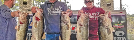 Two anglers proudly display their large bass catches outdoors.