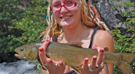 Woman with colorful dreadlocks holding a large fish outdoors.